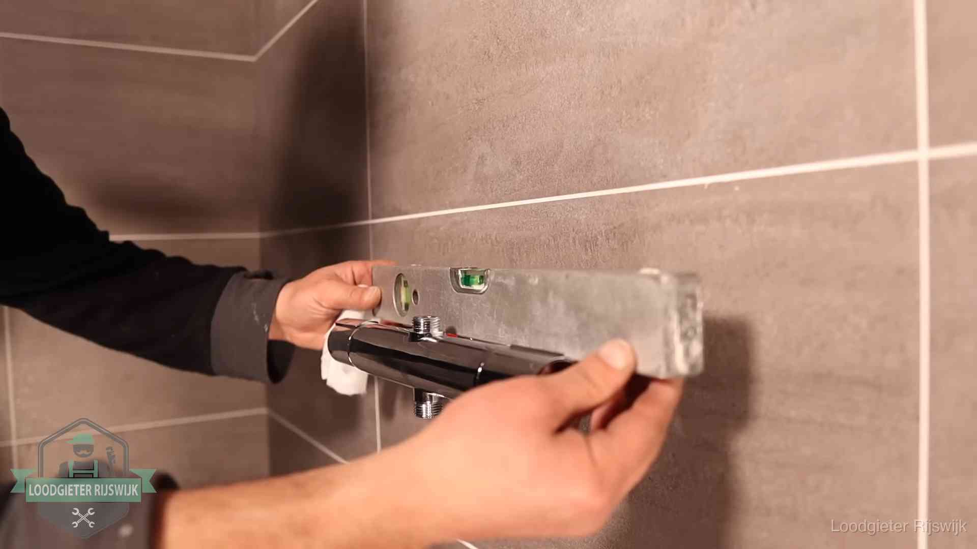 Loodgieter lijnt een douchekraan uit met een waterpas in een woning in Rijswijk