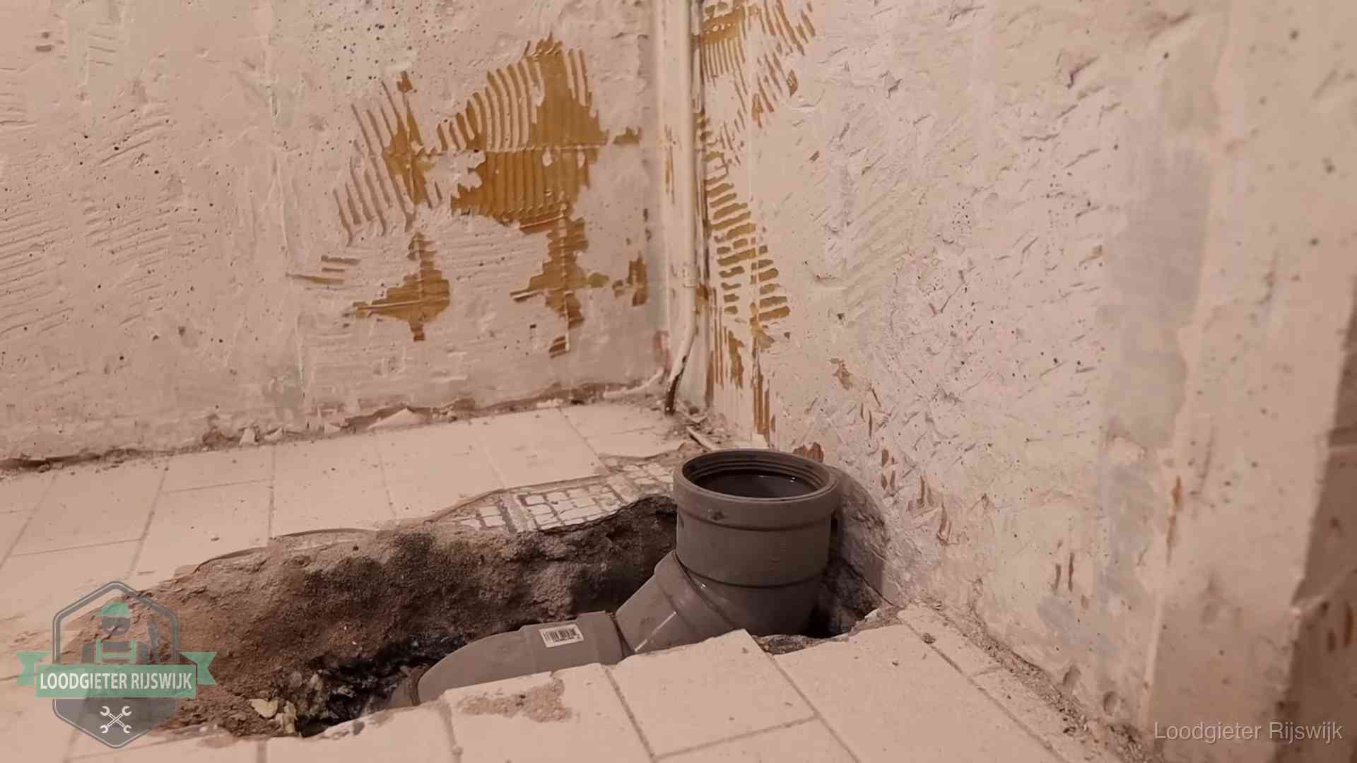 Verzakt riool herstellen in Rijswijk Opengebroken vloer met een nieuwe pvc-rioolbocht in een gegraven sleuf in Rijswijk