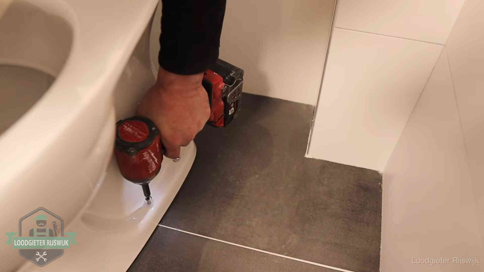 Kosten wc ontstoppen in Rijswijk Loodgieter zet de voet van een wc-pot vast op de tegelvloer in Rijswijk